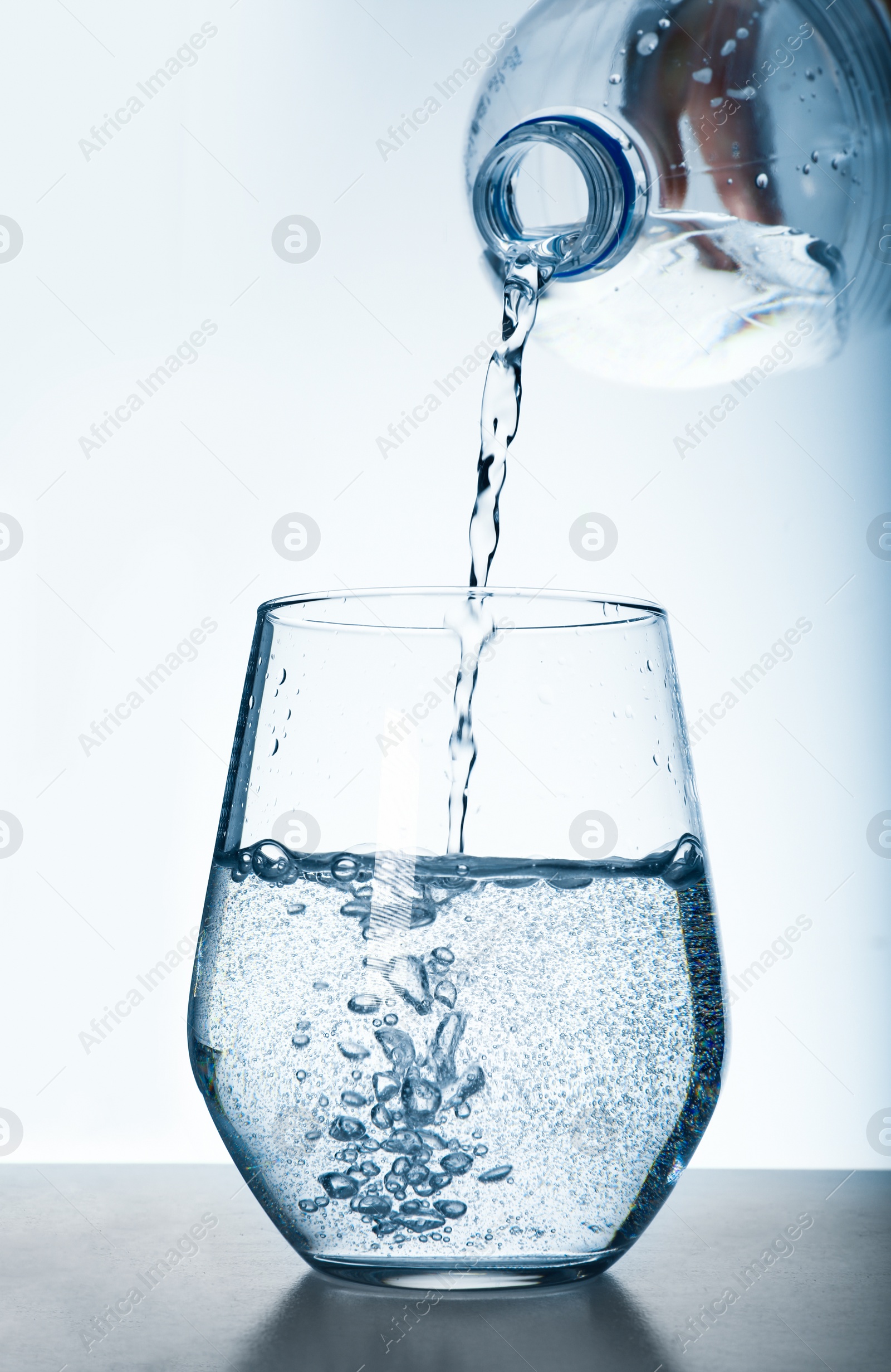 Photo of Pouring water from bottle into glass against grey background. Refreshing drink