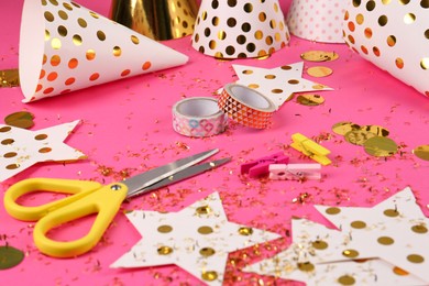 Photo of Party hats with confetti, paper stars, scissors and tapes on pink background. Handmade decorations