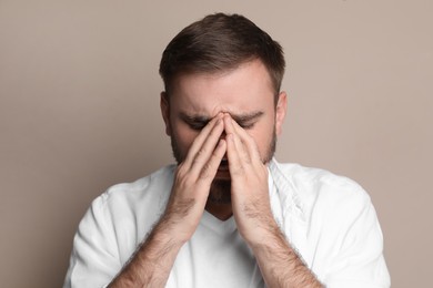 Young man suffering from headache on beige background