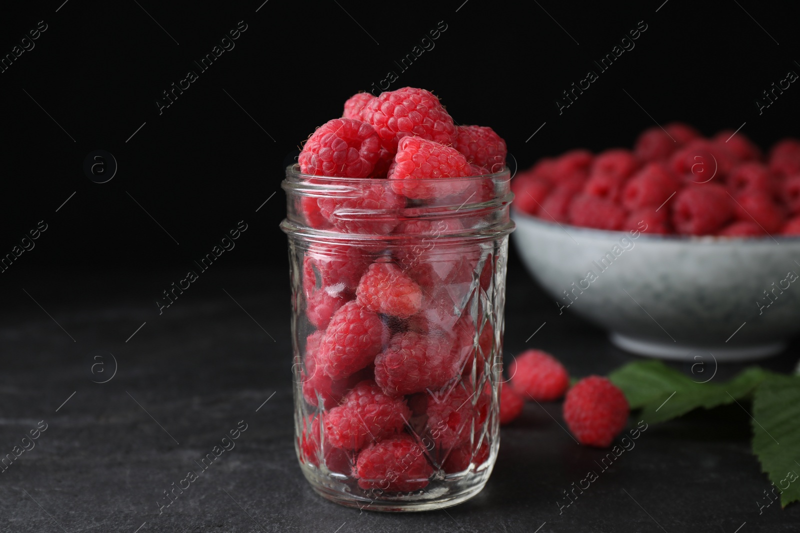 Photo of Delicious fresh ripe raspberries in glass jar on black table