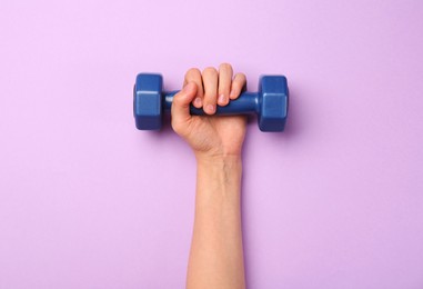 Photo of Woman holding blue dumbbell on violet background, top view