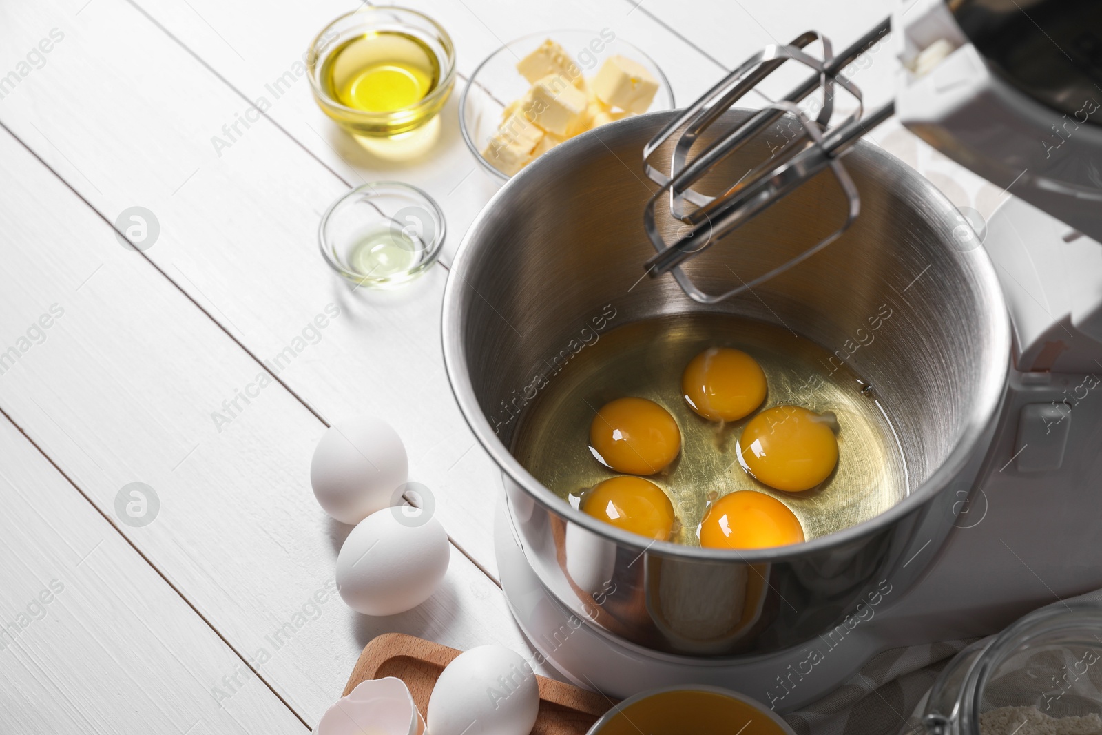 Photo of Making dough. Raw eggs in bowl of stand mixer and ingredients on white wooden table, space for text