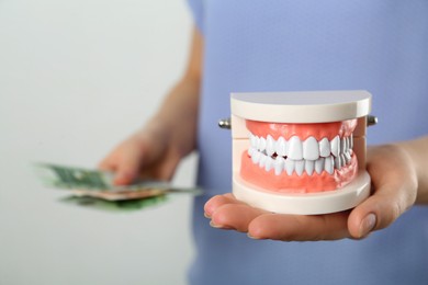 Photo of Woman holding educational dental typodont model and money on light background, closeup. Expensive treatment