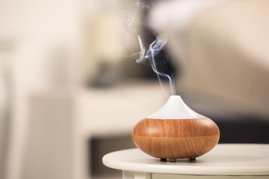 Photo of Modern essential oil diffuser on table indoors. Space for text