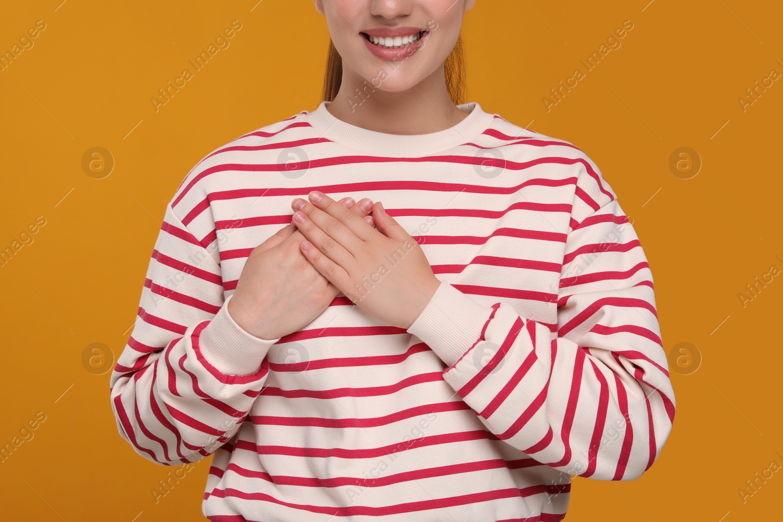 Photo of Thank you gesture. Grateful woman with hands on chest against orange background, closeup