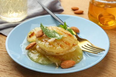 Tasty grilled pineapple slices served with mint and almonds on wooden table, closeup