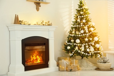 Decorated Christmas tree with faux fur skirt and gift boxes near fireplace indoors