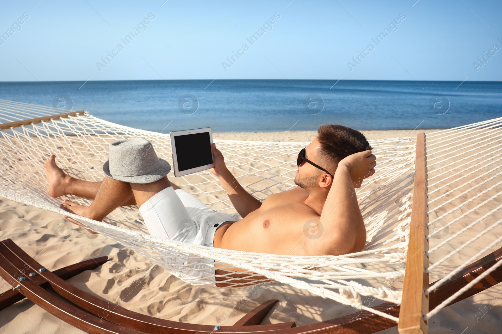 Photo of Young man with tablet in hammock on beach