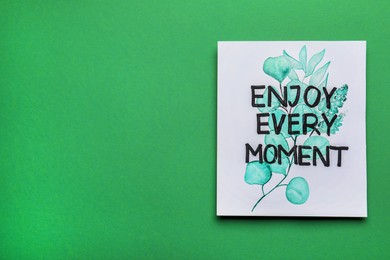 Photo of Card with beautiful phrase Enjoy Every Moment on green background, top view. Space for text