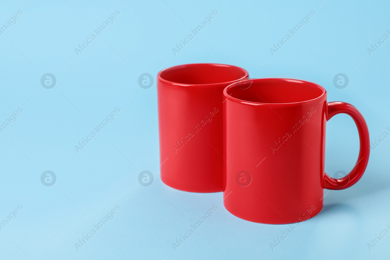 Photo of Two red ceramic mugs on light blue background. Space for text