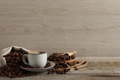 Photo of Cup of aromatic hot coffee and beans on wooden table, space for text