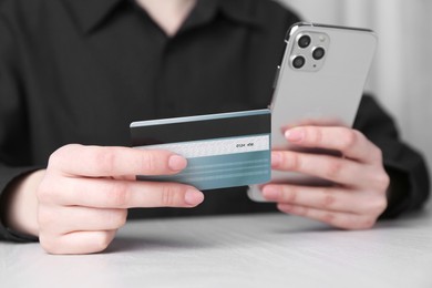 Photo of Online payment. Woman with smartphone and credit card at white wooden table, closeup