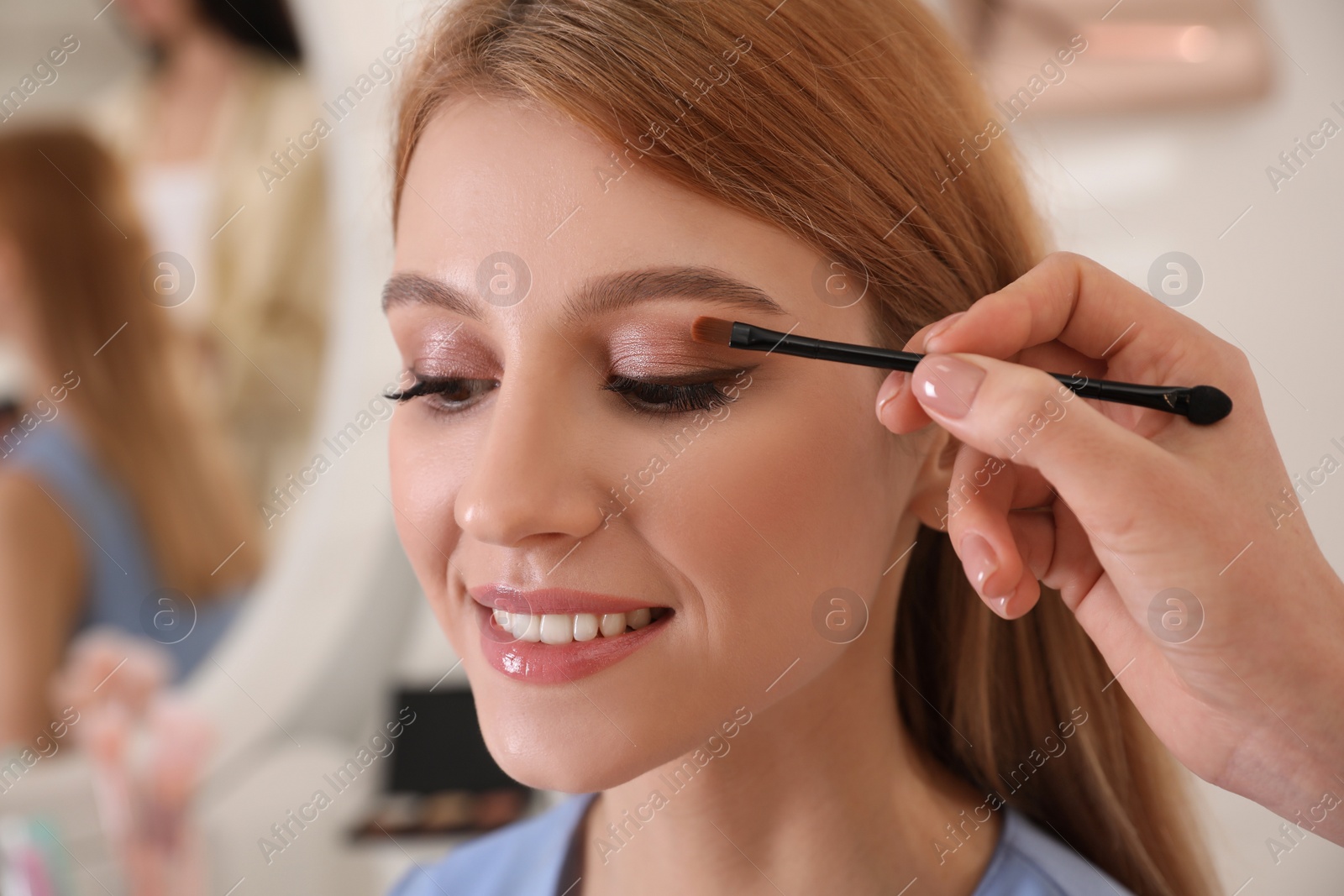 Photo of Professional makeup artist working with beautiful woman in salon