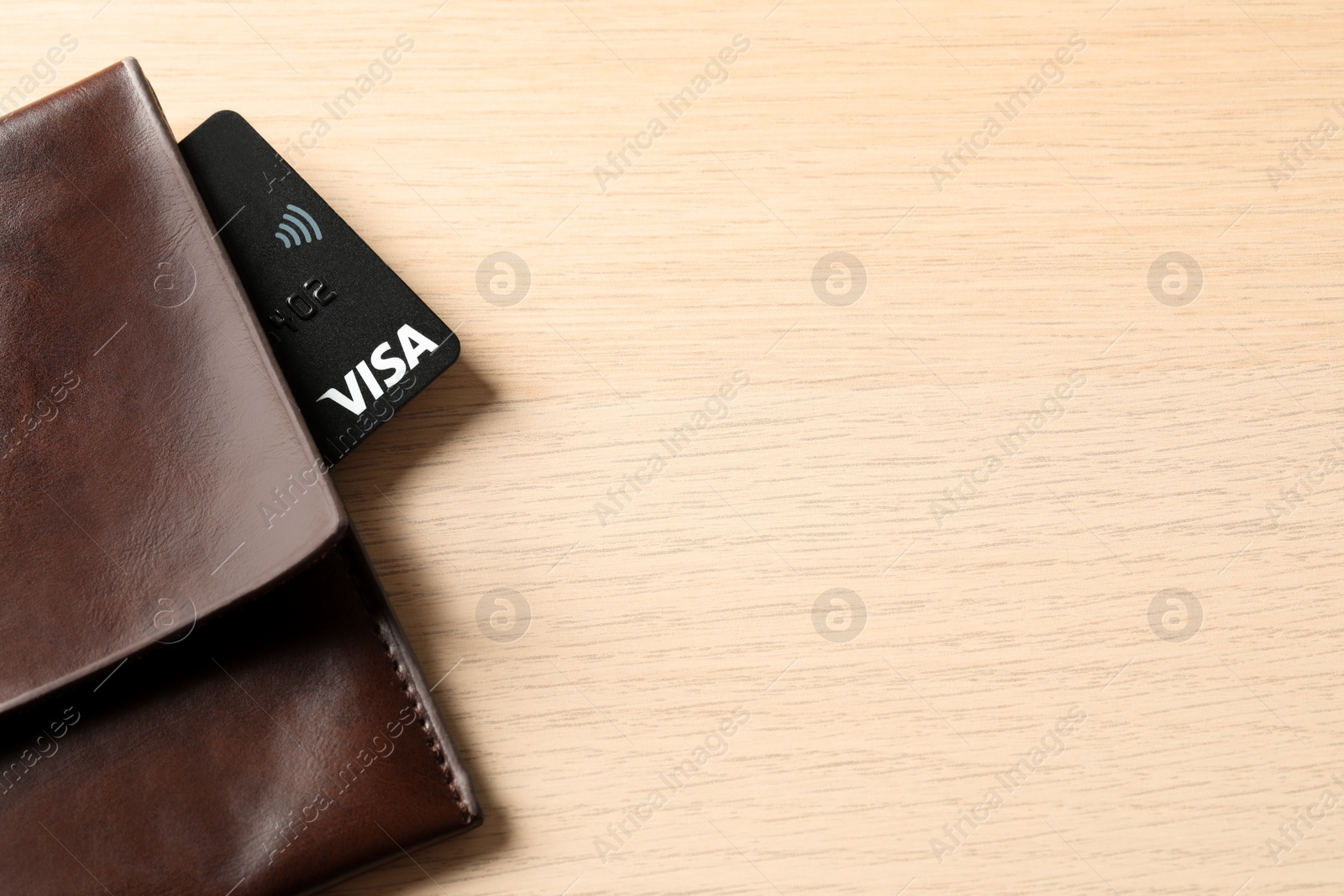 Photo of MYKOLAIV, UKRAINE - FEBRUARY 23, 2022: Bank card of Visa payment system in leather wallet on wooden table, top view. Space for text