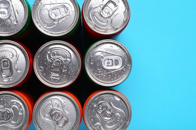 Photo of Energy drinks in wet cans on light blue background, top view. Space for text