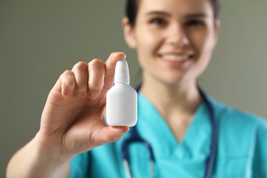 Photo of Woman holding nasal spray bottle on olive background, selective focus. Space for text