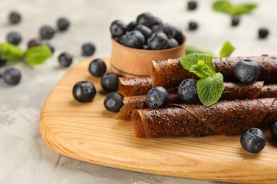 Photo of Delicious fruit leather rolls and blueberries on grey table, closeup