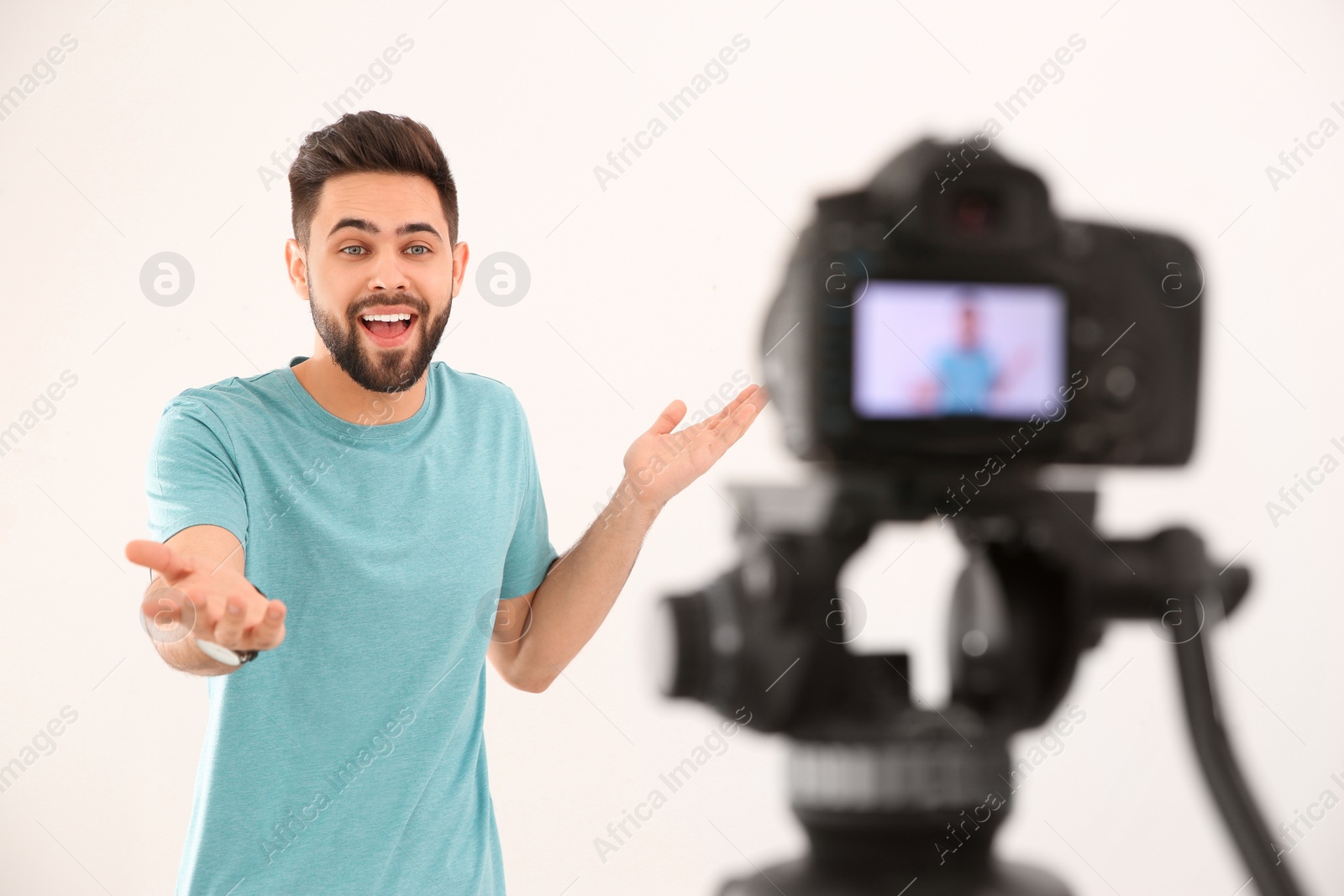 Photo of Young blogger recording video on camera against white background