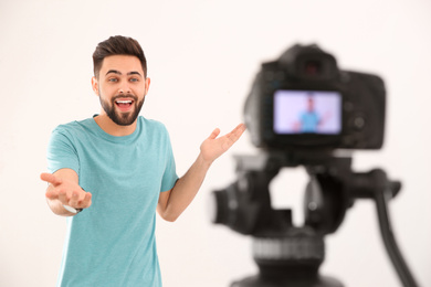 Young blogger recording video on camera against white background