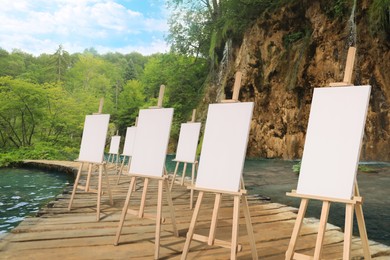 Image of Wooden easels with blank canvases near river on sunny day 