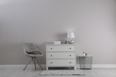 Stylish room interior with white chest of drawers and comfortable chair