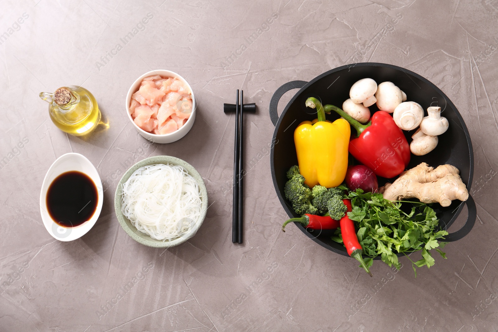 Photo of Wok, chopsticks and different products on grey textured table, flat lay