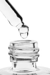 Dripping clear facial serum from pipette into glass bottle on white background, closeup