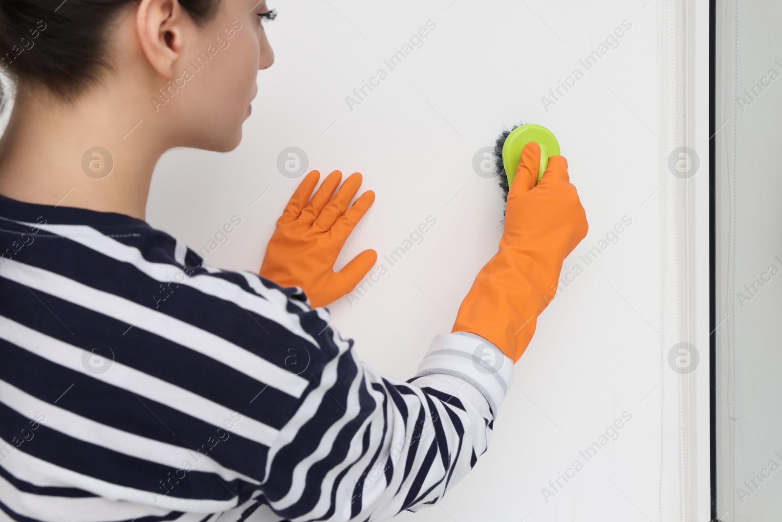 Photo of Woman in rubber gloves cleaning wall with brush indoors, closeup