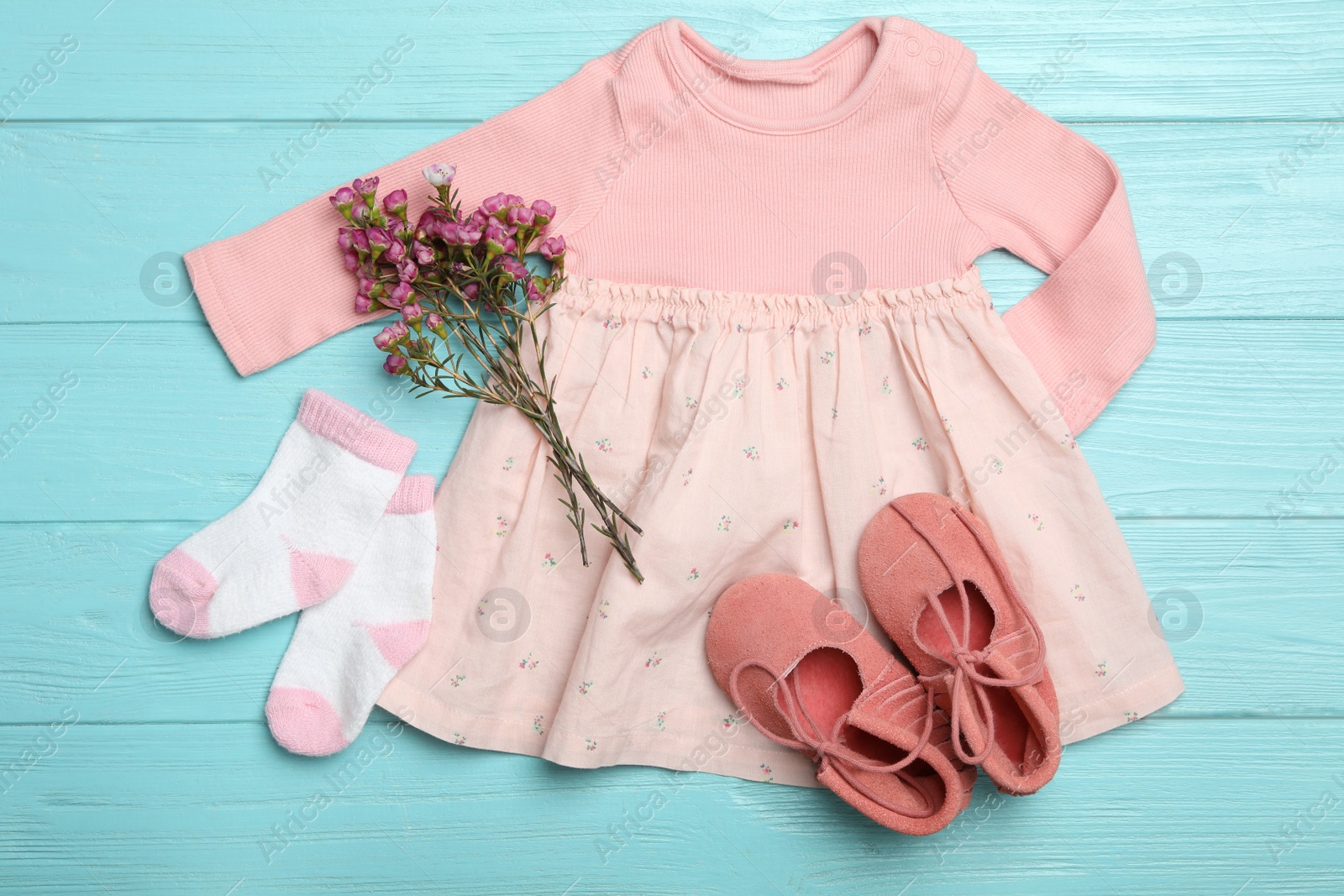 Photo of Flat lay composition with child's clothes and flowers on light blue wooden table