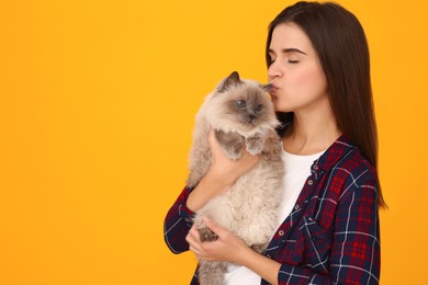 Photo of Woman kissing her cute cat on orange background, space for text