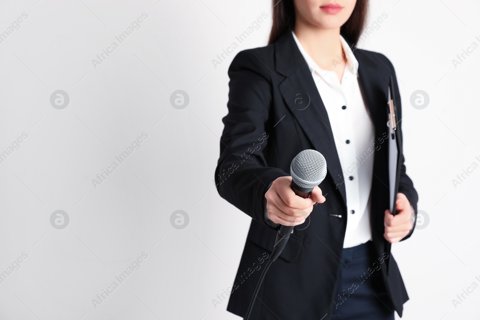 Photo of Young businesswoman holding microphone and clipboard on color background. Space for text