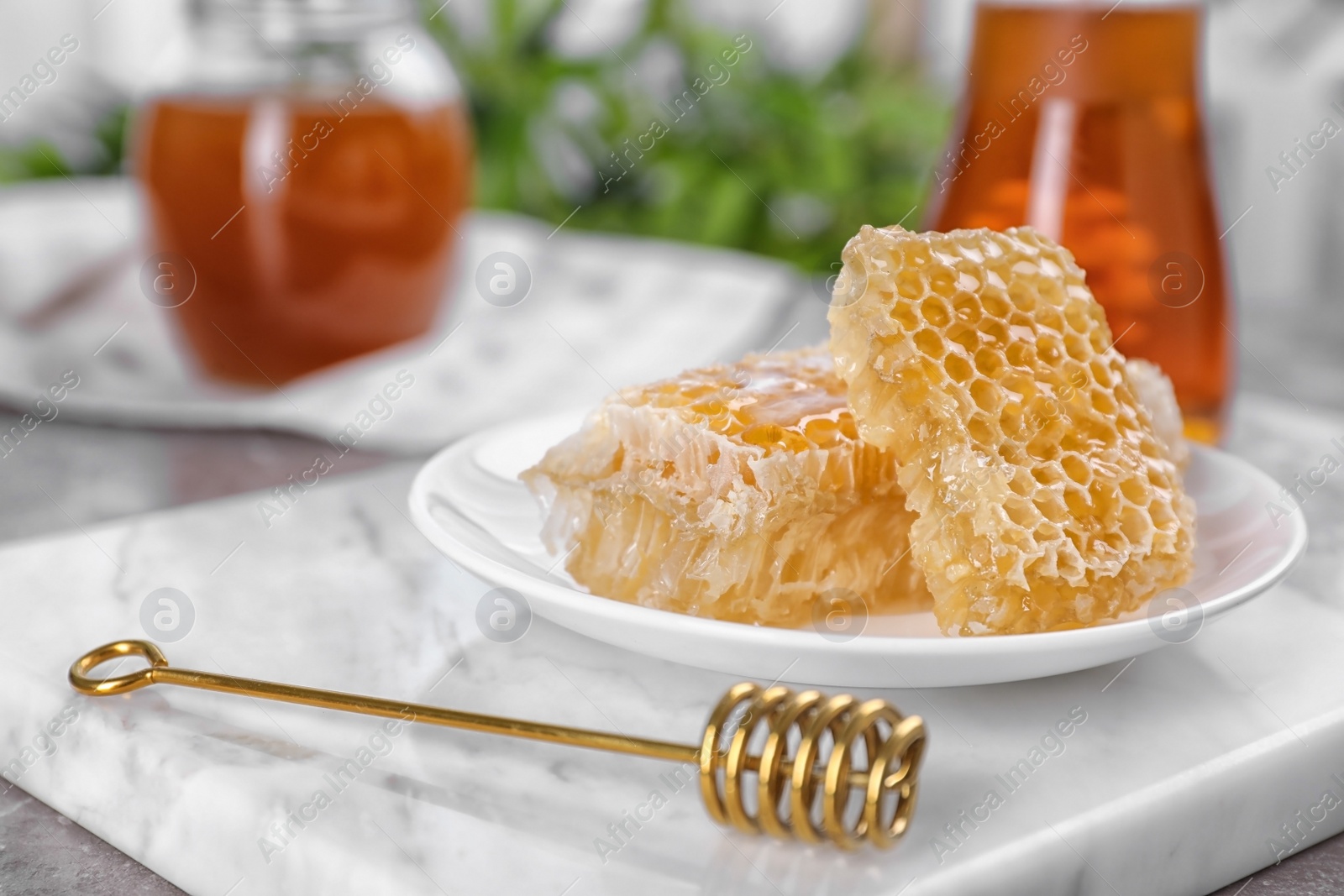 Photo of Plate with fresh honeycombs and dipper on marble board, closeup