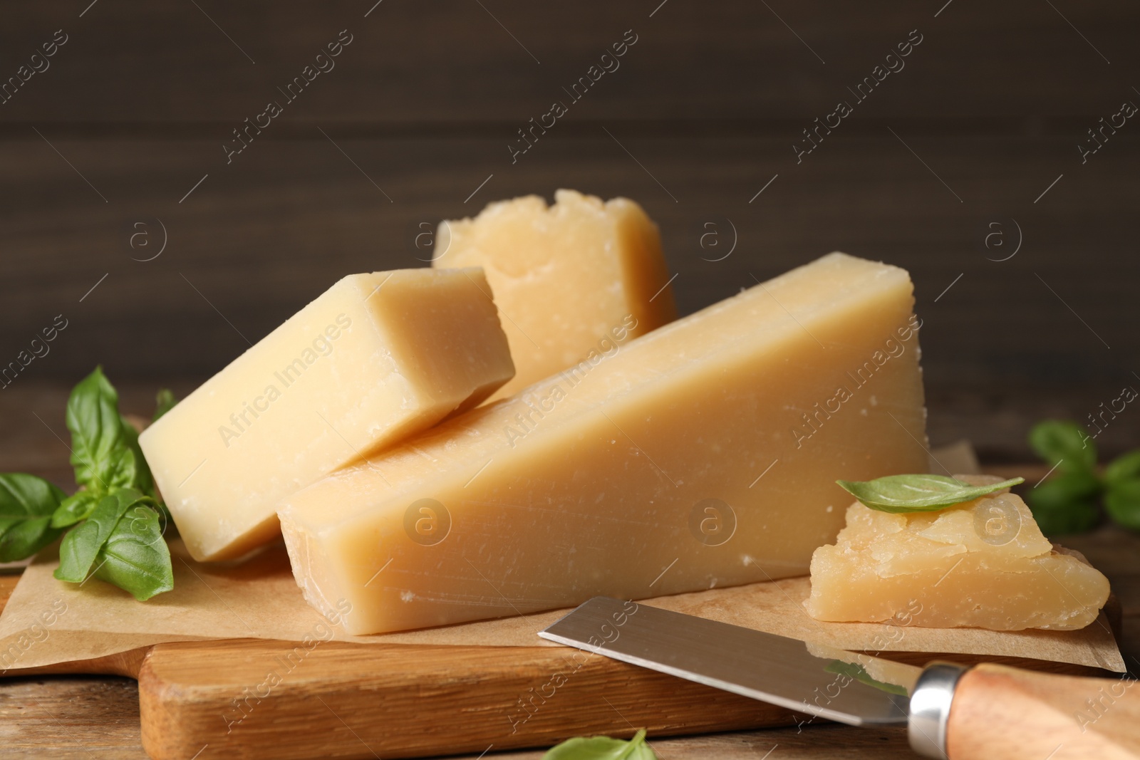 Photo of Delicious parmesan cheese with basil and knife on wooden table, closeup