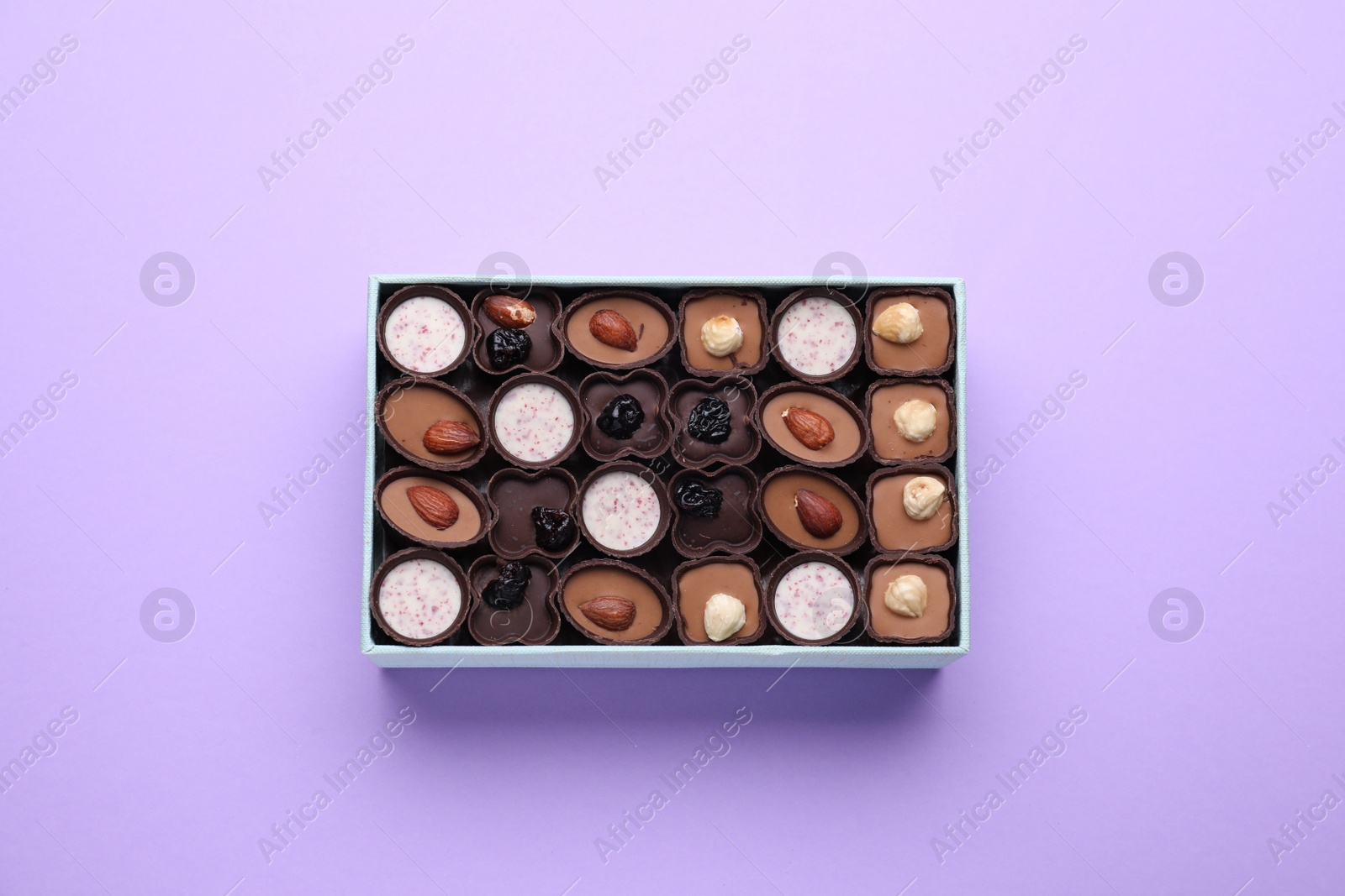 Photo of Box of delicious chocolate candies on violet background, top view