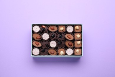 Photo of Box of delicious chocolate candies on violet background, top view