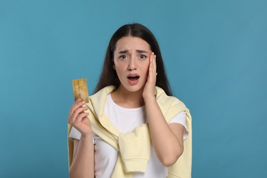 Shocked woman with credit card on light blue background. Debt problem