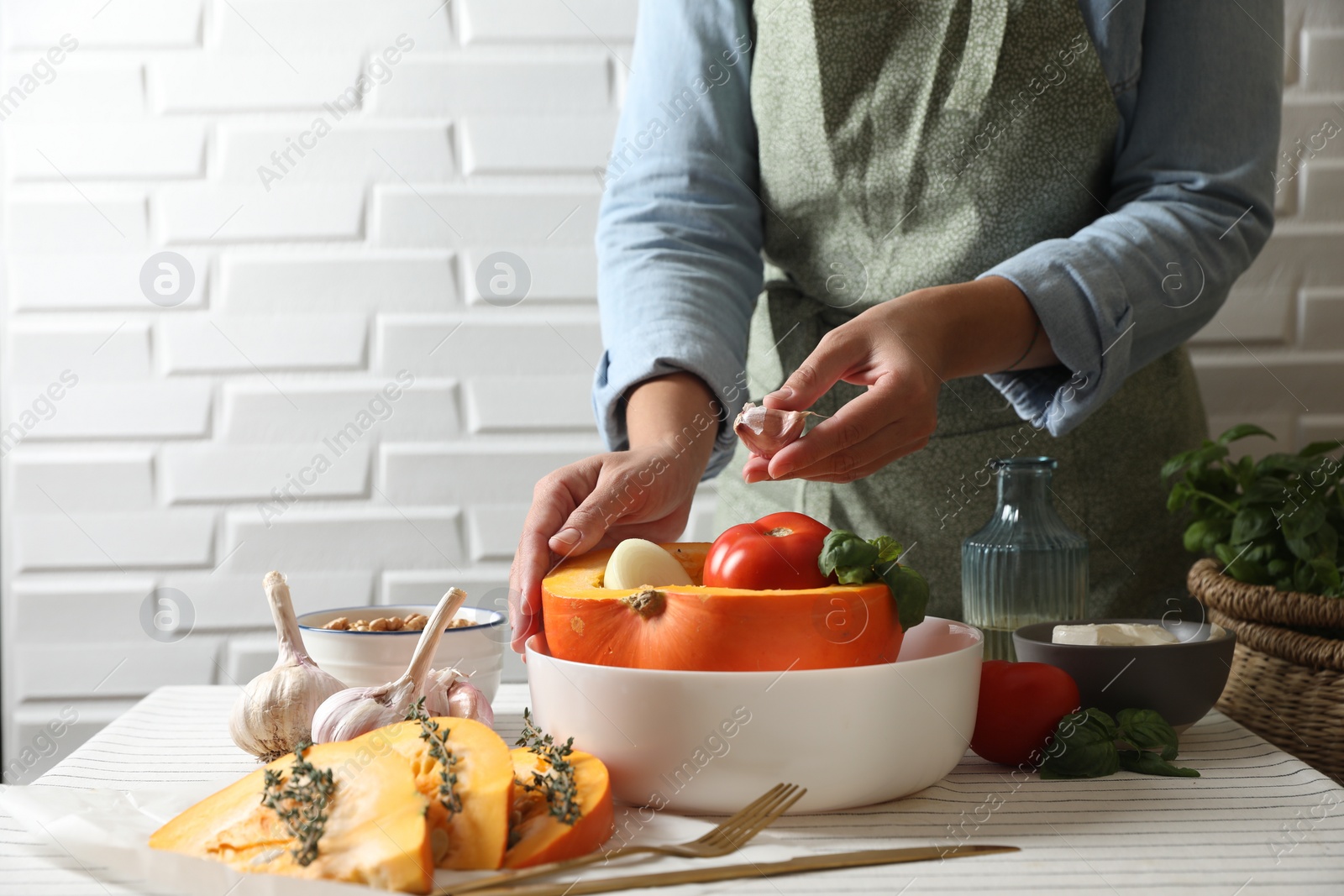 Photo of Woman stuffing pumpkin with vegetables at table, closeup