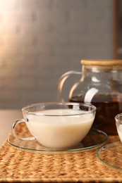 Tasty milk in glass cup on wicker mat, space for text