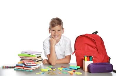 Cute boy sitting at table with school stationery against white background