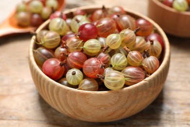 Bowl of fresh ripe gooseberries on wooden table, closeup