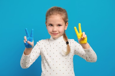 Photo of Little girl with hands painted in Ukrainian flag colors on light blue background. Love Ukraine concept