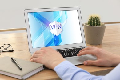 Image of Man using laptop with switched on VPN at wooden table indoors, closeup
