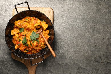 Delicious chicken curry in frying pan and spoon on grey table, top view. Space for text
