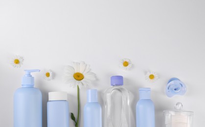 Photo of Different skin care products for baby in bottles and daisies on white background, flat lay. Space for text