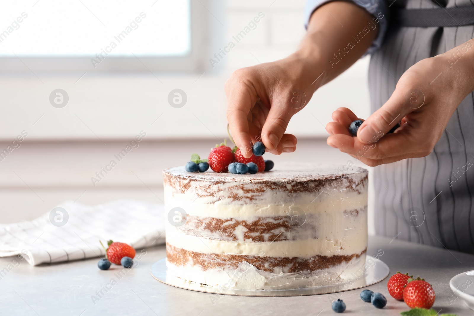 Photo of Woman decorating delicious cake with fresh berries at table. Homemade pastry