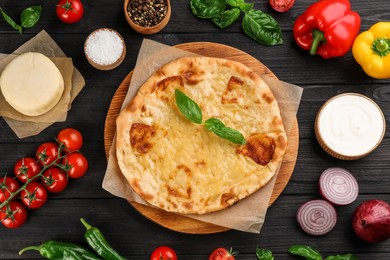 Photo of Delicious khachapuri with cheese, sauce, vegetables and spices on dark wooden table, flat lay