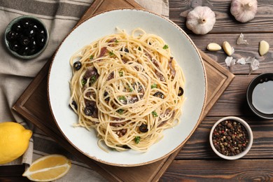 Delicious pasta with anchovies, olives and parmesan cheese served on wooden table, flat lay