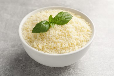 Bowl with grated parmesan cheese and basil on grey table, closeup