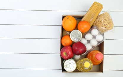 Photo of Humanitarian aid. Different food products for donation in box on white wooden table, top view. Space for text