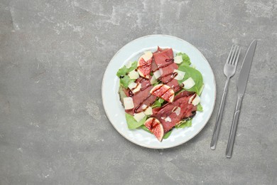 Photo of Plate with delicious bresaola salad served on grey textured table, flat lay. Space for text